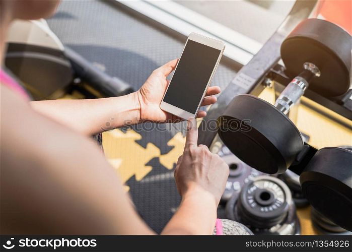 Young asian sportswoman sitting and using smartphone in gym. Young asian woman using smartphone in gym
