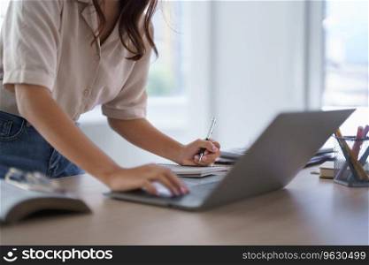 Young asian student in casual clothes watching tutorial and studying lecturer education online class with laptop digital technology while typing research knowledge data and taking notes in notebook.