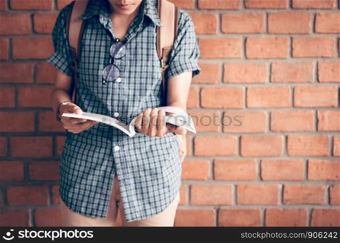 Young asian student studying in library with brick wall background.