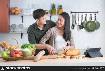 Young Asian sweet couple cooking together in home kitchen. Handsome man helping holding beautiful woman hand slicing bread for preparing meal, making salad, fresh fruits for breakfast. Romantic lover