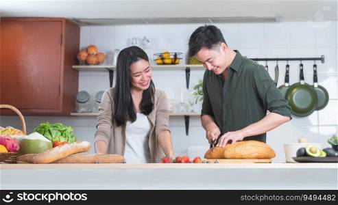 Young Asian sweet couple lover cooking together in home kitchen. Beautiful woman smiling and looking at handsome man preparing meal, slicing bread, making salad, fresh fruits and juice for breakfast