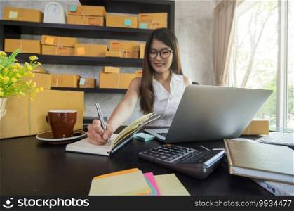 Young asian teenager owner business woman work at home for online shopping, writing the order and prepaing package the product with office equipment, entrepreneur and alpha generation life style concept