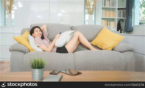 Young Asian teenager woman watching TV at home, female feeling happy lying on sofa in living room. Lifestyle woman relax in morning at home concept.