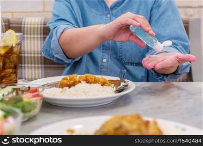 Young Asian woman applying hand sanitizer onto her hand before eating in restaurant for protection against infectious virus, bacteria and germs. Coronavirus Covid-19, health care concept.