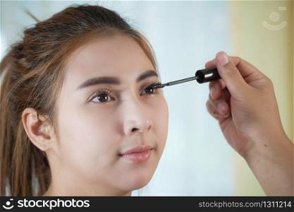 Young asian woman applying mascara on her long eyelashes