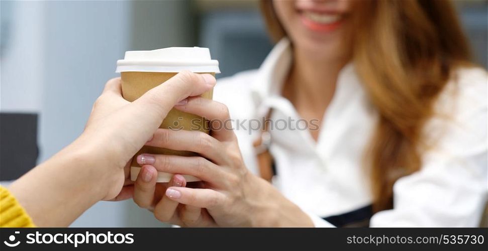 Young asian woman barista serving a disposable coffee cup with smiling face at cafe counter background, small business owner, food and drink industry