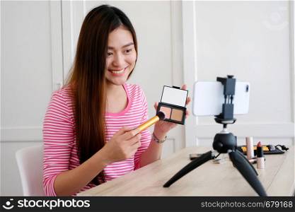 Young asian woman beauty blogger showing how to make up video tutorial while recording by smartphone