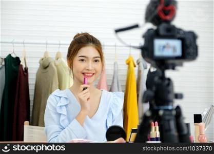 Young asian woman beauty video blogger showing lipstick for make up, beauty fashion vlog concept, people and technology communication