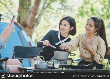 Young asian woman cooking and her friend enjoy to make the meal in pot, They are talk and laugh with fun together while c&ing in nature park