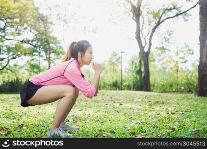 Young asian woman do squats for exercise to build up her beauty . Young asian woman do squats for exercise to build up her beauty body in park environ with green trees and warm sunlight in the afternoon. Young woman workout exercise at the park. Outdoor exercising.