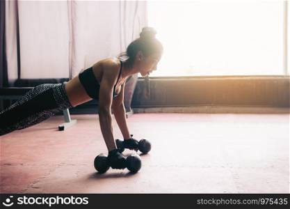 Young asian woman doing push-ups on dumbbell in a gym.