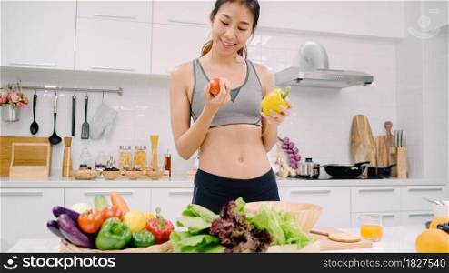 Young Asian woman drink orange juice making salad in the kitchen, beautiful female in sport clothing use organic fruits and vegetables making healthy food by herself at home. Healthy food concept.
