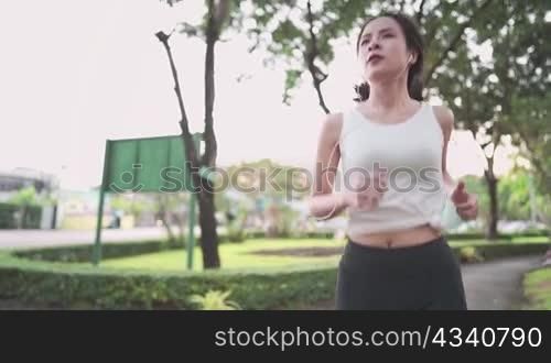 Young asian woman earphone jogging at the park grass during morning marathon training program, protection from virus, holding protective face mask, stay strong during pandemic, healthy lifestyle
