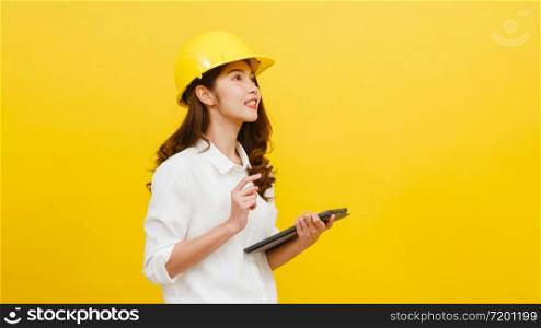 Young Asian woman engineer using digital tablet with positive expression, dressed in casual clothing and looking at camera over yellow background. Happy adorable glad woman rejoices success.