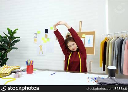Young asian woman fashion designer stretching body for relaxing while working in home studio, small business owner, fashion industry concept