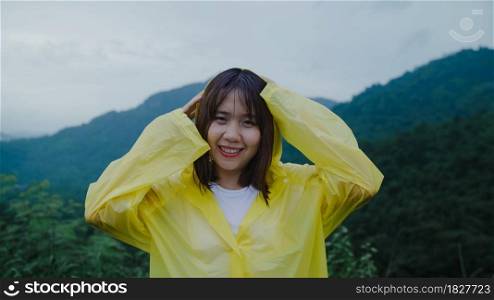 Young Asian woman feeling happy playing rain while wearing raincoat walking near forest. Lifestyle women enjoy and relax in rainy day.