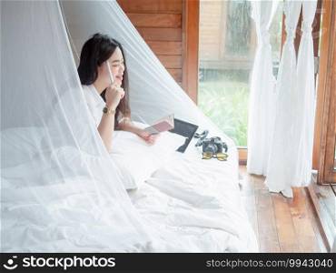 Young Asian woman freelance working on notebook and tablet remotely while rest in bedroom of resort during summer vacations.