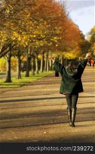 Young Asian woman happy in autumn park with open arms in the hair. Shot from behind