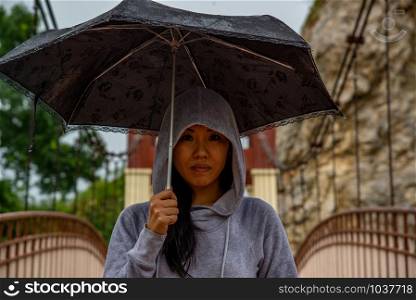 Young asian woman hold Umbrella and crossing on a wooden bridge on a rainy day. Close-up