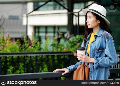 Young asian woman holding a take away paper coffee cup while standing outdoors city background, food and drink business concept, people lifestyle