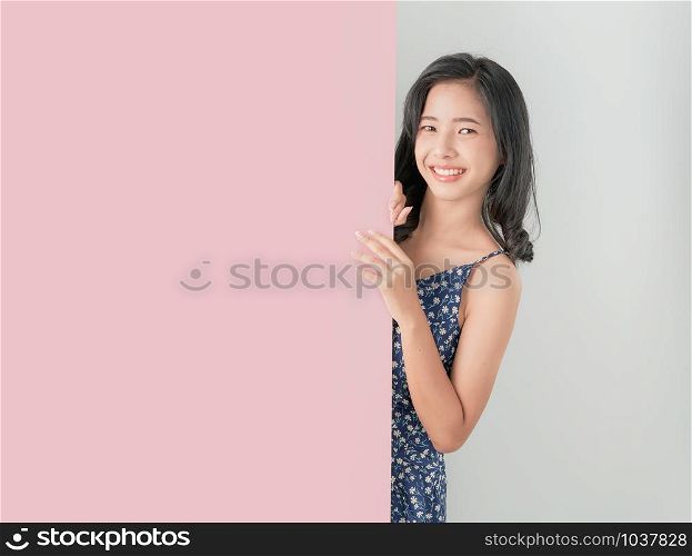 Young Asian woman holding blank paper with smiling face and looking on the gray background. for advertising signs.