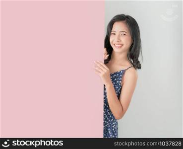 Young Asian woman holding blank paper with smiling face and looking on the gray background. for advertising signs.