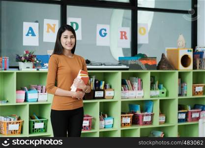Young asian woman holding books standing at library background, education concept