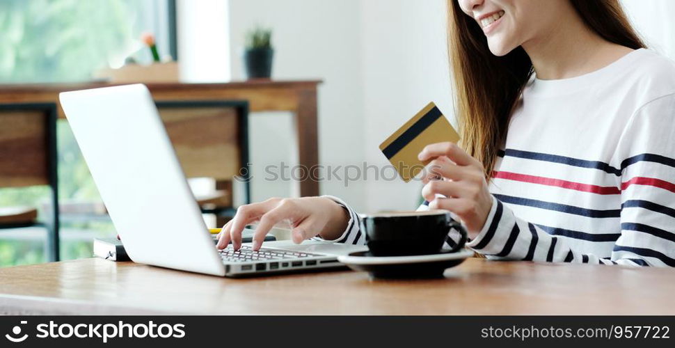 Young asian woman holding credit card and using laptop computer for shopping on line at cafe, business and technology concept, digital marketing, casual lifestyle