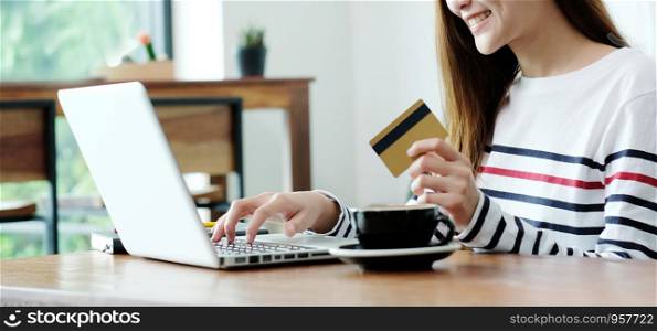 Young asian woman holding credit card and using laptop computer for shopping on line at cafe, business and technology concept, digital marketing, casual lifestyle
