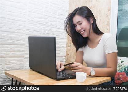 Young asian woman holding credit card and using laptop computer to shopping on line at cafe