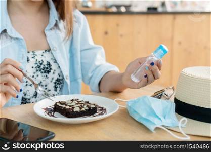 Young Asian woman holding hand sanitizer onto her hand while eating with in cafe. Protection against infectious virus, bacteria and germs. Coronavirus Covid-19, health care concept.