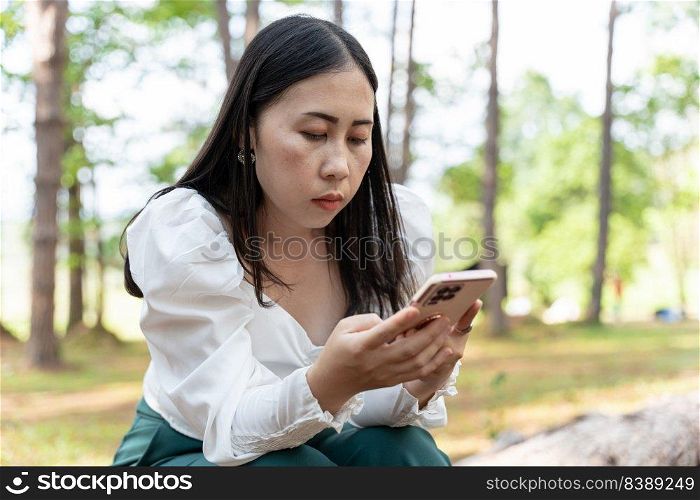 Young Asian woman holding mobile phone in park. Searching or social networks concept.