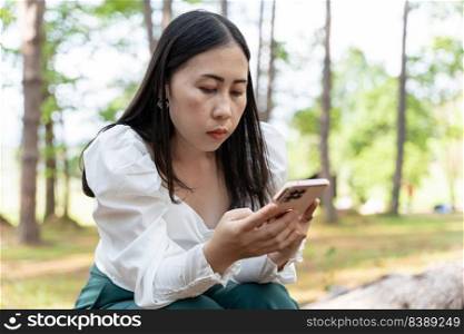 Young Asian woman holding mobile phone in park. Searching or social networks concept.