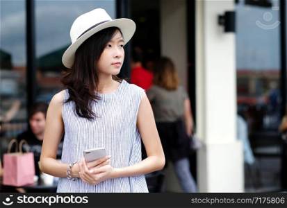 Young asian woman holding smartphone while standing in front of cafe in the city outdoors background, people working outdoors with technology, urban lifestyle, people on phone