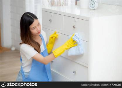 Young asian woman in gloves cleaning home in room, housekeeper is wipe with fabric, housemaid and service, worker polish dust at living room in house, housework and domestic, lifestyle concept.
