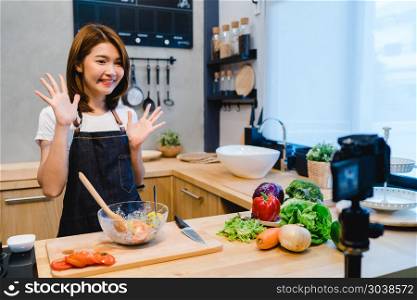 Young asian woman in kitchen recording video on camera. Smiling . Young asian woman in kitchen recording video on camera. Smiling asian woman working on food blogger concept with fruits and vegetables in kitchen .
