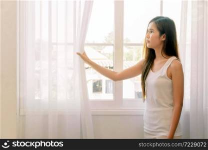 Young asian woman looking outside and feeling depress stress. She stay isolation at home for self quarantine. Corona virus outbreak situation. Self quarantine at home prevention COVID-19.