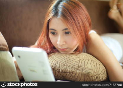 Young asian woman lying on sofa and using a tablet