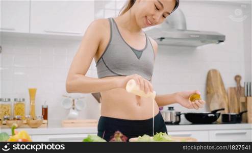 Young Asian woman making salad healthy food while using mobile phone for looking recipe in the kitchen, beautiful female use vegetables preparing salad for fit body at home. Healthy food concept.