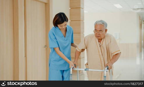 Young Asian woman nurse caregiver assistance encourage take care her senior patient explain with positive keep comforting for practice walker in hospital ward, Hospital environment concept.