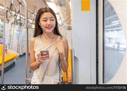 Young Asian woman passenger listening music via smart mobile phone in subway train when traveling in big city,japanese,chinese,Korean lifestyle and daily life, commuter and transportation concept