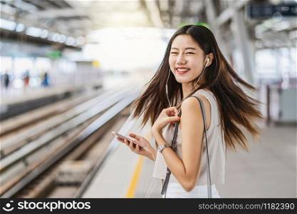 Young Asian woman passenger listening music via smart mobile phone with happiness action in subway train station, japanese,chinese,Korean lifestyle, commuter and transportation concept
