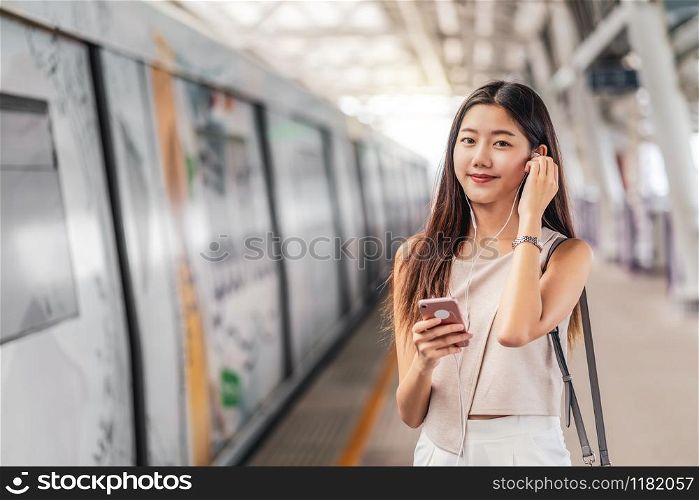 Young Asian woman passenger using and listening music via smart mobile phone in subway train station, japanese,chinese,Korean lifestyle, leisure and daily life, commuter and transportation concept