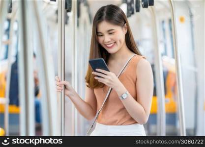 Young Asian woman passenger using smart mobile phone and looking to outside of subway train when traveling in big city, commuter and transportation concept