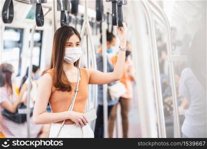 Young Asian woman passenger wearing surgical mask and listening music via smart mobile phone in subway train when traveling in big city at Covid19 outbreak, Infection and Pandemic concept