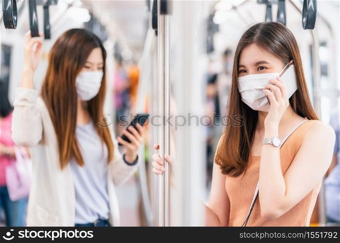 Young Asian woman passenger wearing surgical mask and talking together via smart mobile phone in subway train when traveling in big city at Covid19 outbreak, social distancing and new normal concept