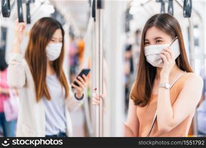 Young Asian woman passenger wearing surgical mask and talking together via smart mobile phone in subway train when traveling in big city at Covid19 outbreak, social distancing and new normal concept