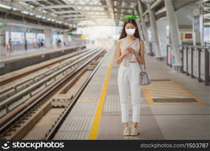 Young Asian woman passenger wearing surgical mask and using social network via smart mobile phone in subway train when traveling in big city, commuter and transportation with covid-19 outbreak concept