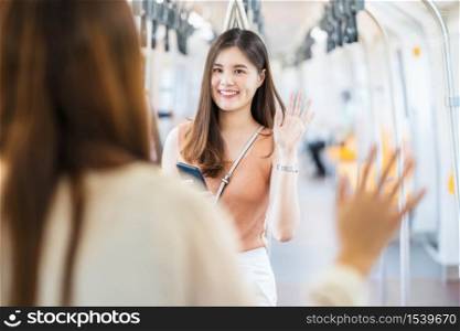 Young Asian woman passenger wearing surgical mask and Waving hand for greeting to her friend in subway train when traveling in big city at Covid19 outbreak, social distancing and new normal concept