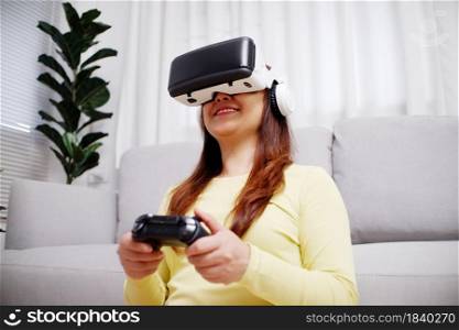 Young asian woman playing video games wearing virtual reality glasses inthe living room